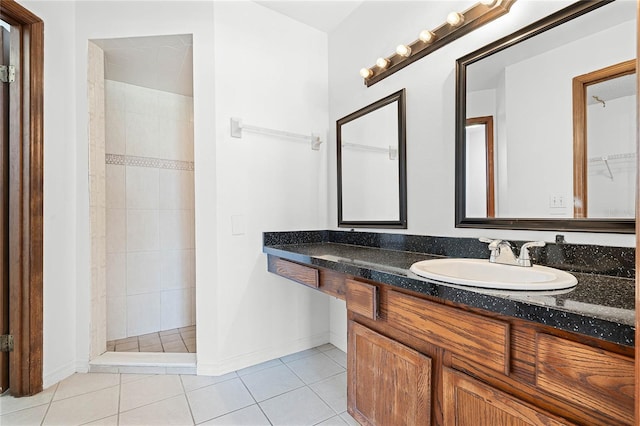 full bath featuring tile patterned flooring, a tile shower, vanity, and baseboards