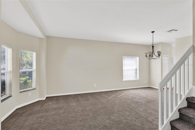 spare room with visible vents, a notable chandelier, dark carpet, baseboards, and stairs