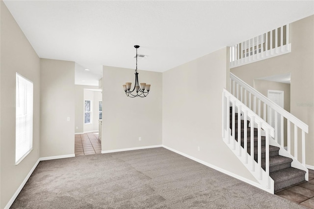 carpeted empty room featuring stairway, baseboards, a healthy amount of sunlight, and a chandelier