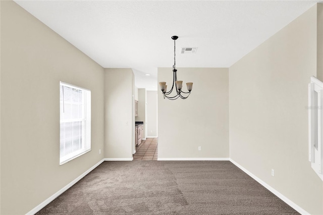 carpeted empty room featuring a notable chandelier, baseboards, and visible vents