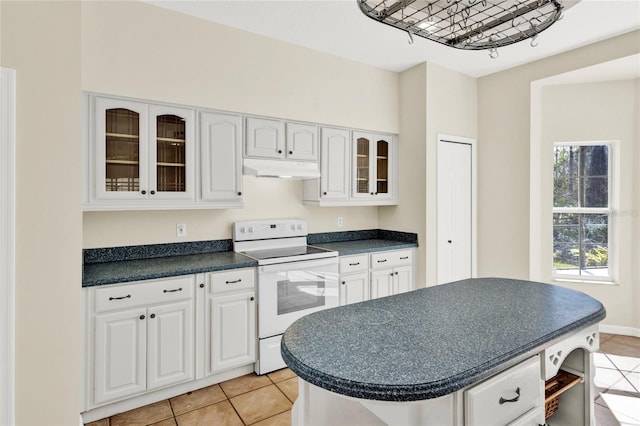 kitchen with white range with electric cooktop, under cabinet range hood, dark countertops, white cabinets, and glass insert cabinets