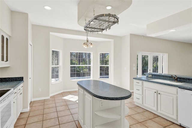 kitchen featuring a wealth of natural light, a notable chandelier, a sink, dark countertops, and white dishwasher