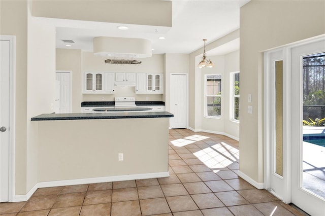 kitchen with light tile patterned floors, glass insert cabinets, under cabinet range hood, white cabinetry, and dark countertops