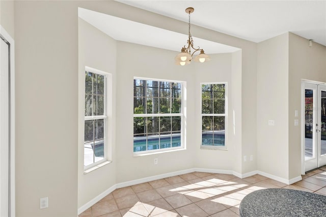 unfurnished dining area featuring a notable chandelier, light tile patterned flooring, and baseboards