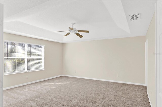 empty room featuring visible vents, baseboards, a tray ceiling, carpet flooring, and a ceiling fan