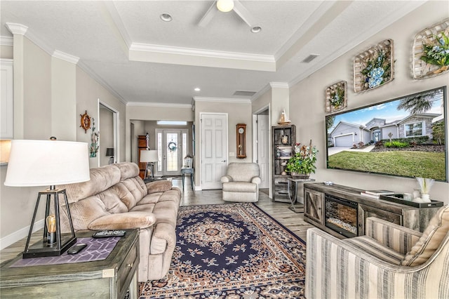 living room with a raised ceiling, crown molding, wood finished floors, and visible vents