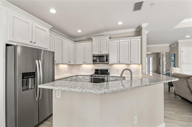 kitchen with light stone countertops, visible vents, a peninsula, stainless steel appliances, and backsplash