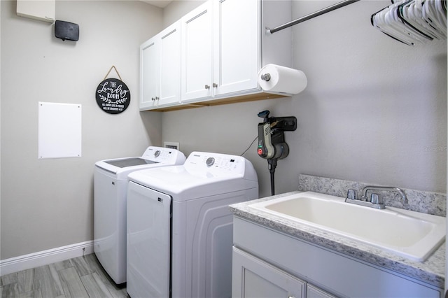 laundry room with light wood-style flooring, a sink, washing machine and dryer, cabinet space, and baseboards