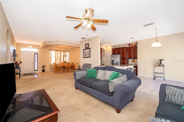 living area featuring light tile patterned floors, visible vents, arched walkways, light carpet, and ceiling fan with notable chandelier