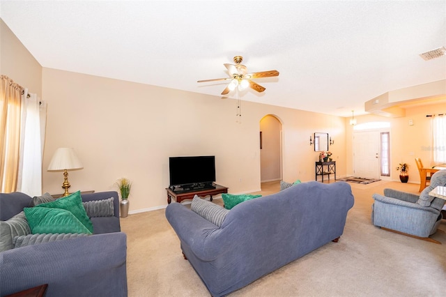 living area with baseboards, visible vents, arched walkways, ceiling fan, and light colored carpet