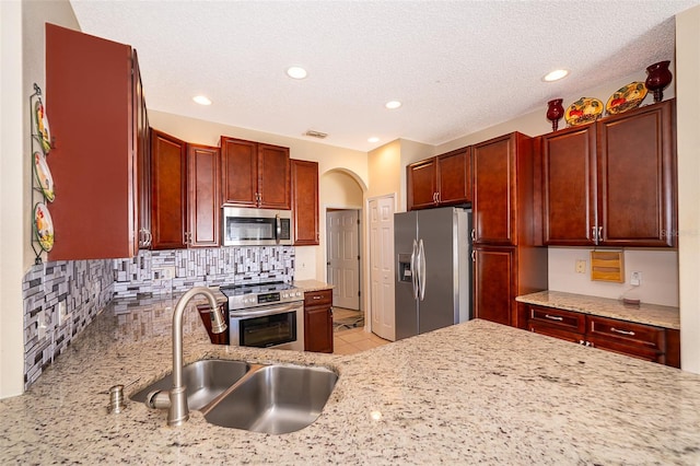 kitchen featuring a sink, stainless steel appliances, light stone counters, and dark brown cabinets