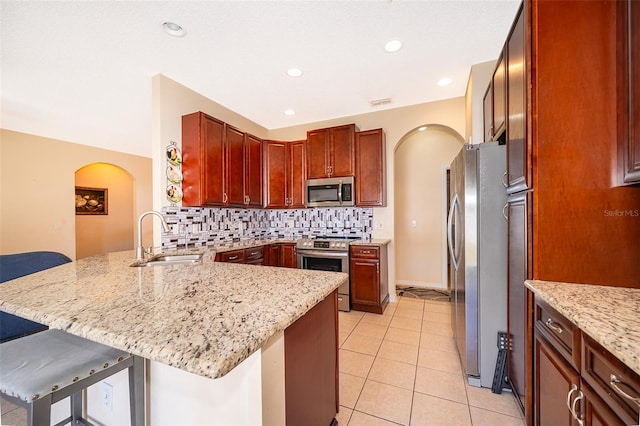 kitchen featuring arched walkways, a peninsula, stainless steel appliances, and a sink