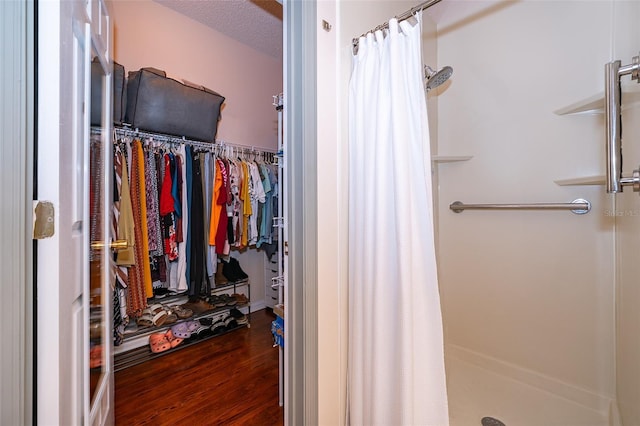 full bath featuring a walk in closet, wood finished floors, a textured ceiling, and a stall shower