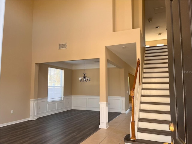 stairs with visible vents, a notable chandelier, a towering ceiling, and wainscoting