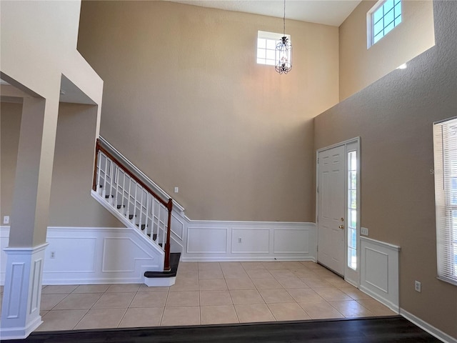 entrance foyer featuring stairs, tile patterned floors, a decorative wall, and a high ceiling