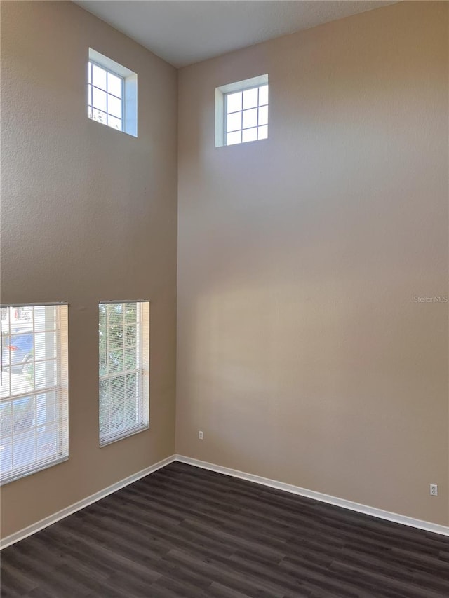unfurnished room featuring a wealth of natural light, baseboards, dark wood-type flooring, and a high ceiling