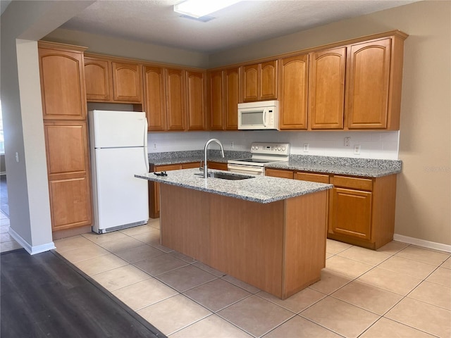 kitchen with white appliances, light tile patterned floors, light stone countertops, a kitchen island with sink, and a sink