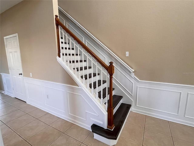 stairs featuring a decorative wall, wainscoting, and tile patterned flooring
