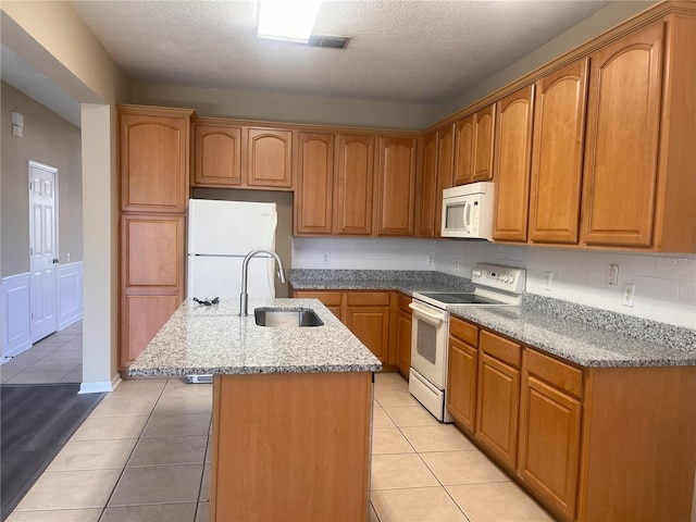 kitchen featuring white appliances, light stone countertops, a center island with sink, and a sink