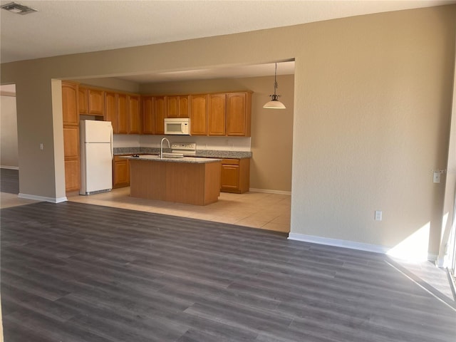 kitchen featuring white appliances, baseboards, visible vents, light wood finished floors, and a center island with sink