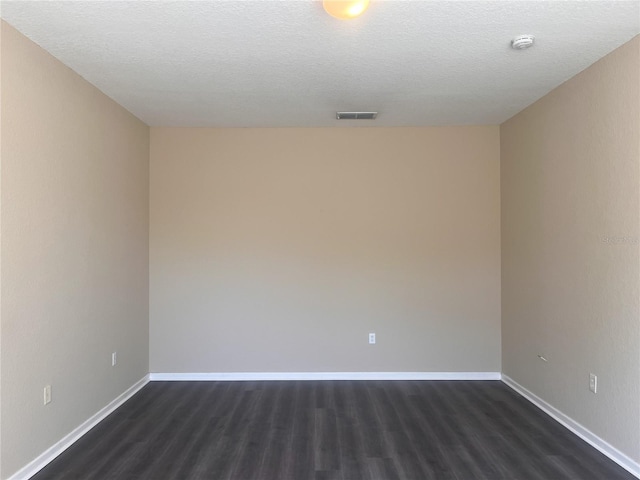 empty room featuring visible vents, baseboards, dark wood-type flooring, and a textured ceiling