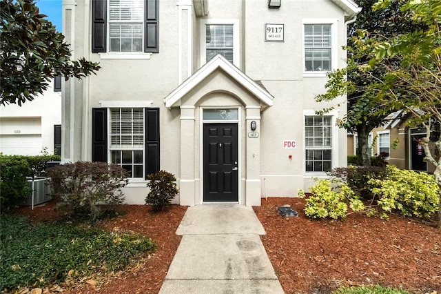 view of exterior entry with central air condition unit and stucco siding