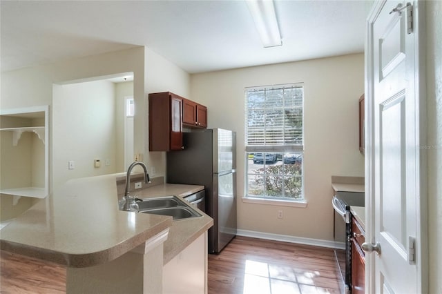 kitchen with a peninsula, a sink, light countertops, electric stove, and light wood-type flooring