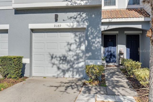 view of exterior entry with a garage, driveway, and stucco siding