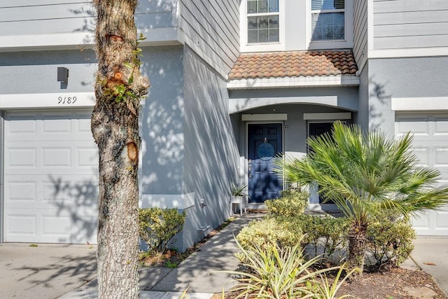 entrance to property featuring a tile roof, a garage, and stucco siding