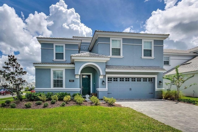 mediterranean / spanish house with stucco siding, a front lawn, a garage, a tiled roof, and decorative driveway