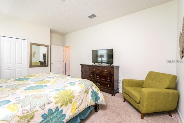 bedroom with a closet, visible vents, light colored carpet, and a textured ceiling