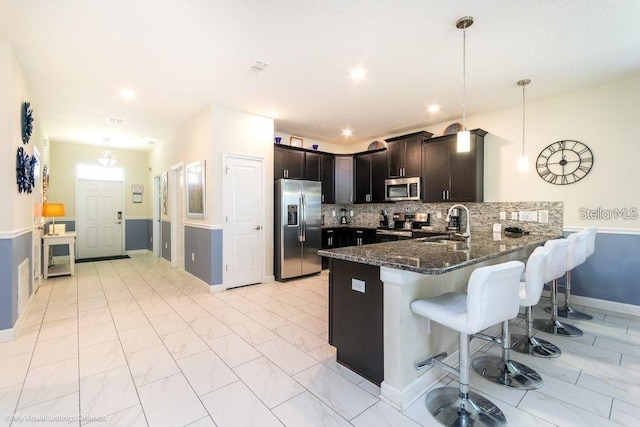 kitchen featuring a peninsula, dark stone counters, a sink, stainless steel appliances, and a kitchen bar