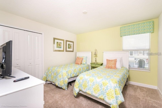 bedroom with a textured ceiling, light colored carpet, a closet, and baseboards