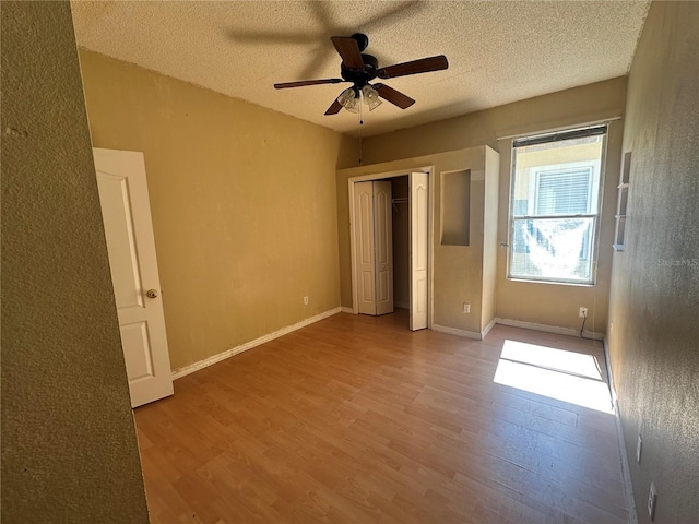 unfurnished bedroom featuring a closet, a textured ceiling, baseboards, and wood finished floors