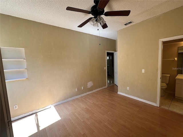 unfurnished bedroom with wood finished floors, baseboards, visible vents, ensuite bathroom, and a textured ceiling