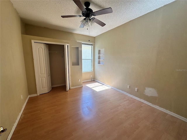 unfurnished bedroom featuring wood finished floors, baseboards, a closet, and a textured ceiling