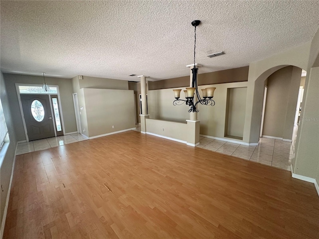 entryway featuring visible vents, a textured ceiling, arched walkways, an inviting chandelier, and light wood finished floors