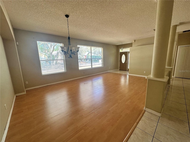 unfurnished dining area with baseboards, a chandelier, light wood-type flooring, decorative columns, and a textured ceiling