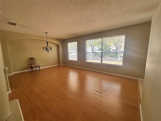 unfurnished dining area featuring visible vents, baseboards, a notable chandelier, and wood finished floors