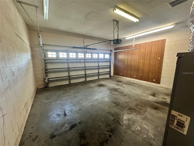 garage with concrete block wall, a garage door opener, and visible vents