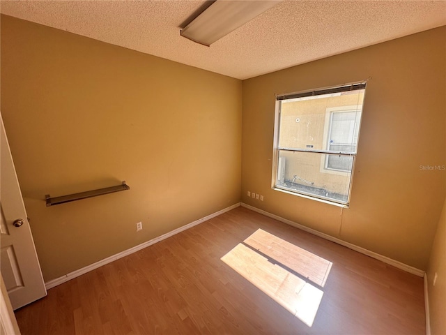 empty room with baseboards, a textured ceiling, and wood finished floors