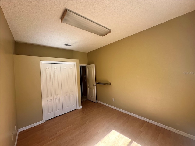 unfurnished bedroom featuring visible vents, baseboards, a textured ceiling, and wood finished floors