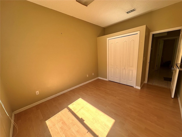 unfurnished bedroom with visible vents, a textured ceiling, wood finished floors, a closet, and baseboards