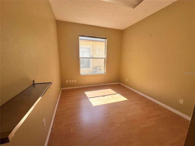 spare room with wood finished floors, baseboards, and a textured ceiling