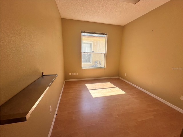 spare room with a textured ceiling, baseboards, and wood finished floors