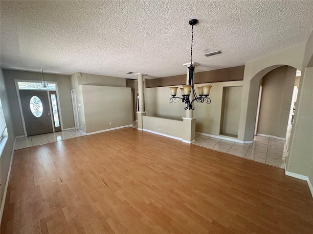 entryway with visible vents, arched walkways, a notable chandelier, and light wood finished floors