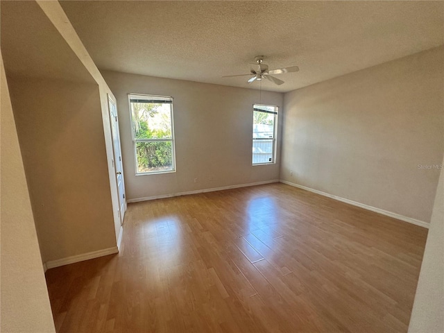 empty room with a textured ceiling, wood finished floors, baseboards, and ceiling fan