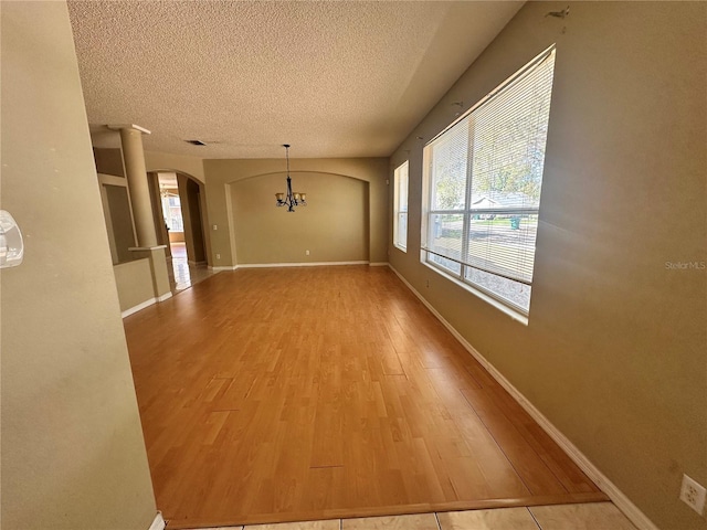 interior space with arched walkways, a chandelier, a textured ceiling, and wood finished floors