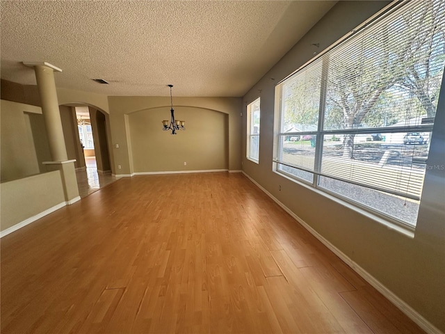 unfurnished dining area with visible vents, light wood-style flooring, an inviting chandelier, arched walkways, and a textured ceiling