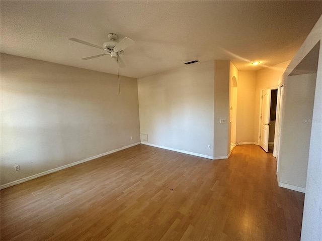 spare room with wood finished floors, a ceiling fan, visible vents, baseboards, and a textured ceiling